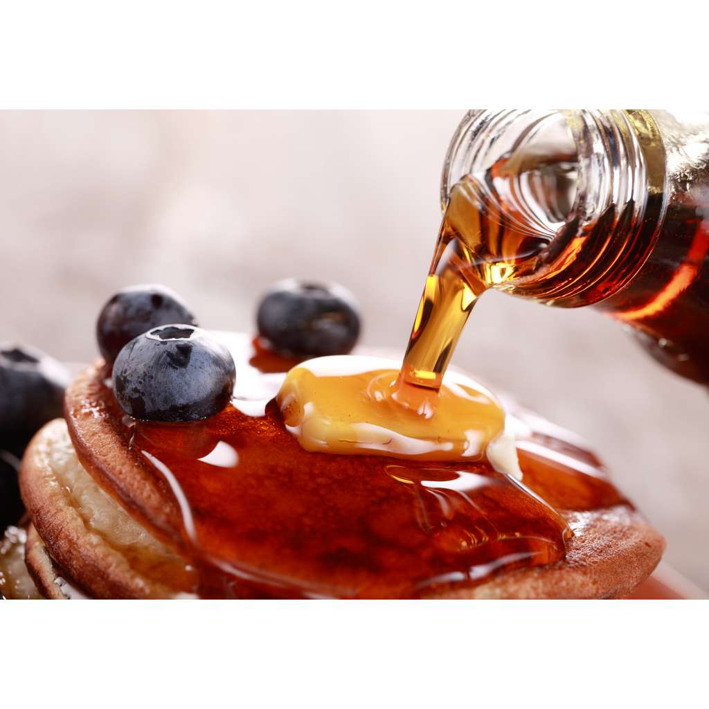 Close-up of pouring maple syrup on stack of pancakes.